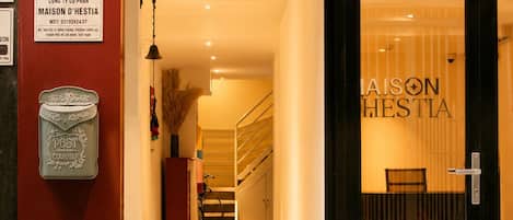 L’entrée d’un hôtel, avec une porte en verre, un escalier menant à l’intérieur et une enseigne indiquant le nom de l’hôtel : « JASON HESTIA ».