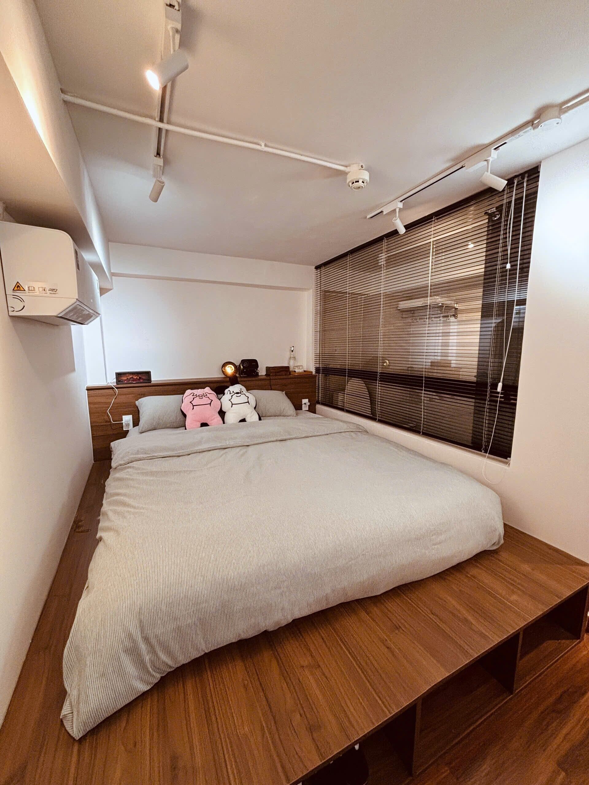 Ein modernes Schlafzimmer mit einem großen Bett, einem Holz-Kopfteil, einem Nachttisch und einem Fenster mit Jalousien.