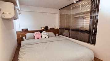 Ein modernes Schlafzimmer mit einem großen Bett, einem Holz-Kopfteil, einem Nachttisch und einem Fenster mit Jalousien.