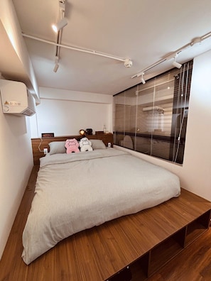 A modern bedroom with a large bed, wooden headboard, bedside table, and a window with blinds. - Maison D'HESTIA Homestay (Ho Chi Minh City)