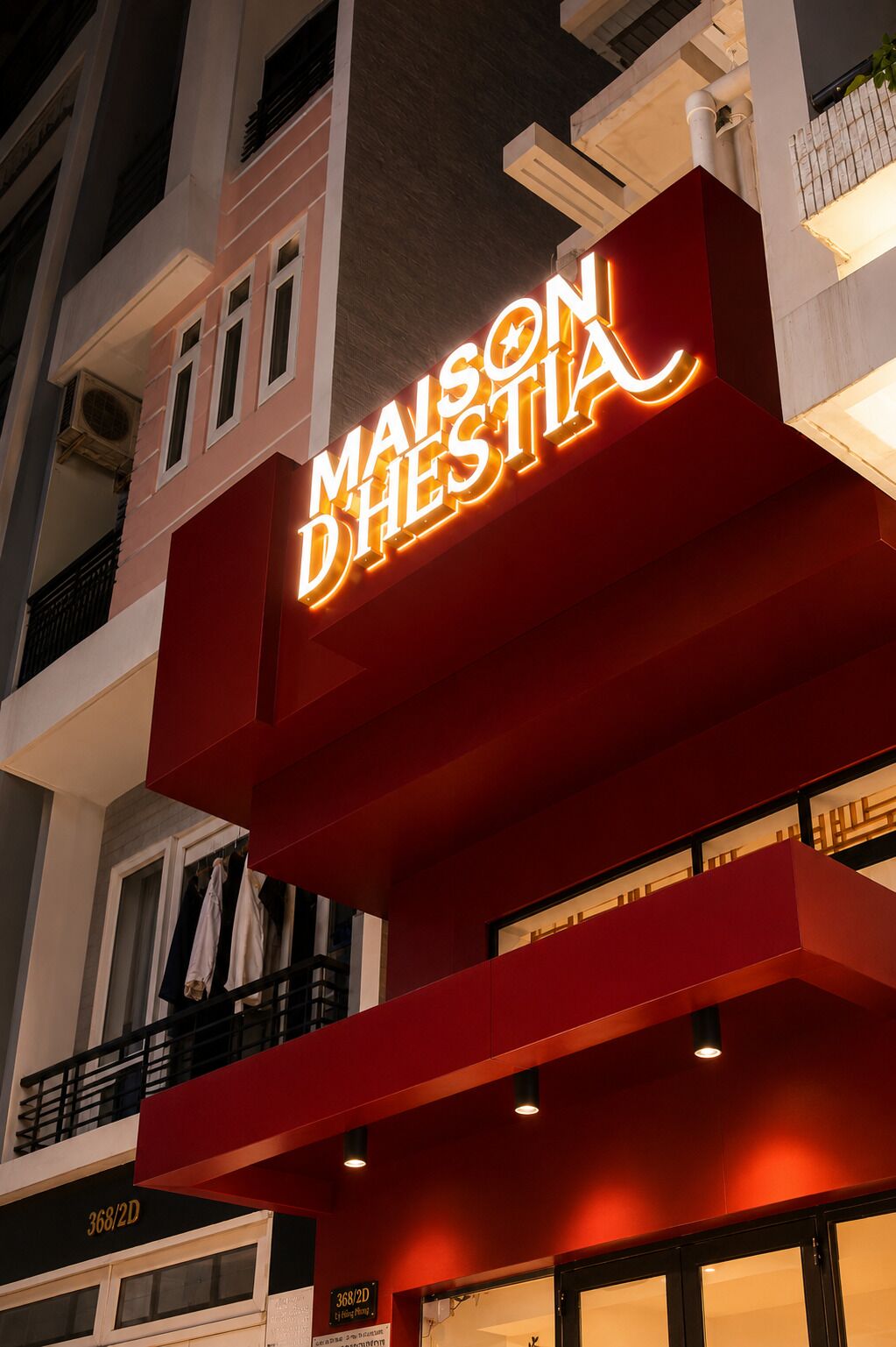 A hotel sign with the name 'MAISON D'HESTIA' illuminated in neon lights.