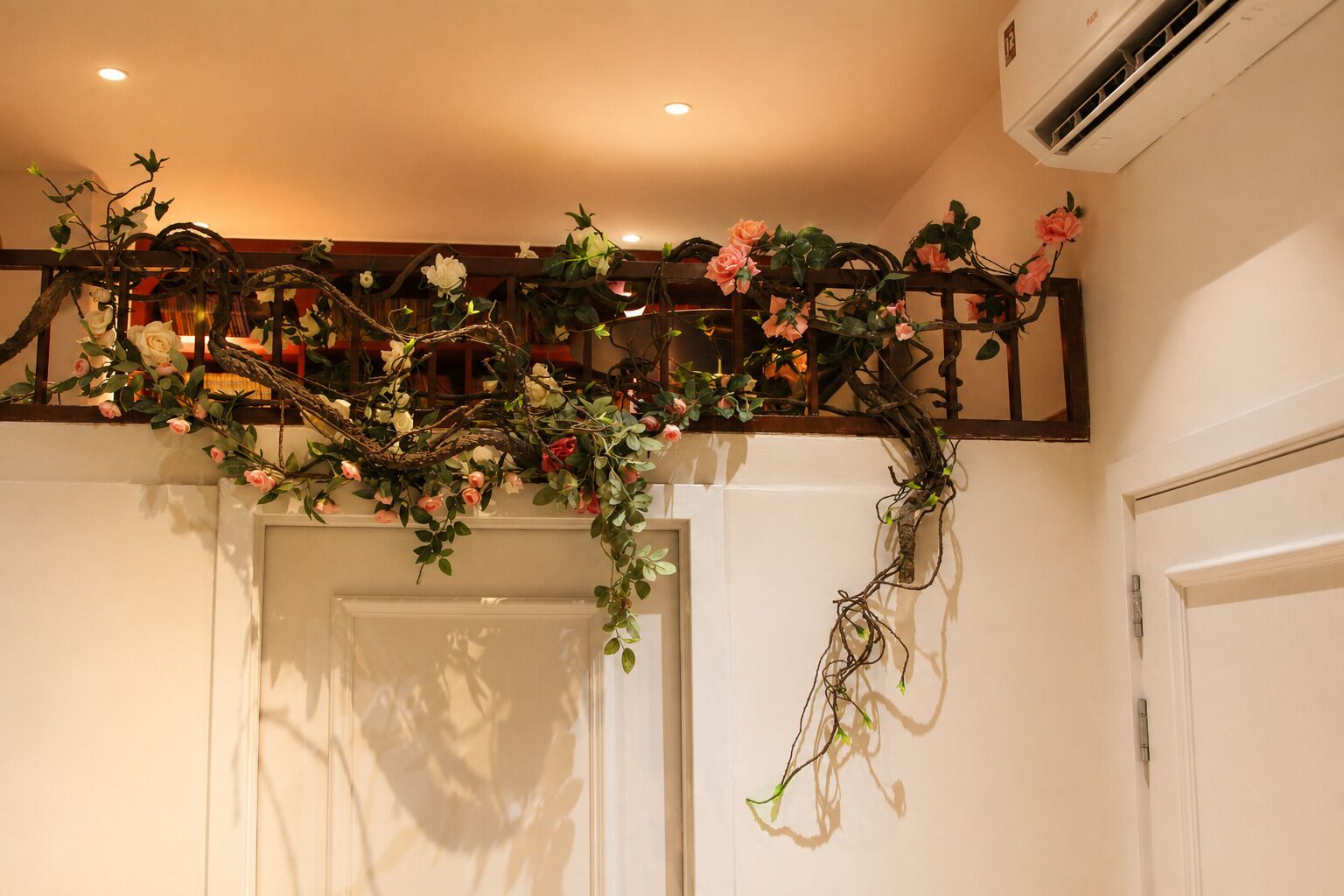 Habitació amb aire condicionat al sostre, una porta blanca i un arranjament floral decoratiu a la paret.