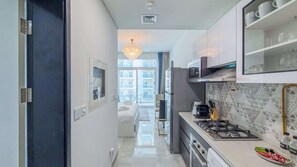 A modern kitchen with a gas stove, microwave, and a view of the cityscape through the window. - Urban Studio Escape at Pearlz Al Furjan (Dubai)