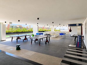 A spacious indoor area with multiple ping pong tables, a foosball table, and a foosball table with a view of the city. - Urban Studio Escape at Pearlz Al Furjan (Dubai)