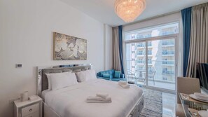 Une chambre d’hôtel comprenant un lit, une table de chevet, une chaise, un coin repas et une grande fenêtre donnant sur des immeubles.