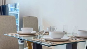 Ein moderner Essbereich mit einem Glastisch, weißen Tellern, Schüsseln und klaren Gläsern.