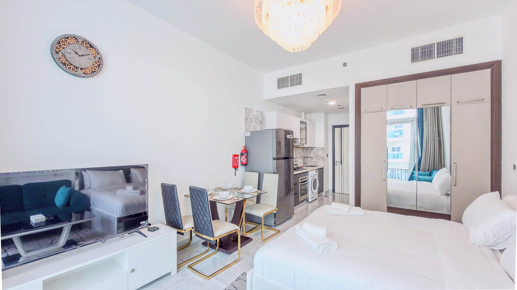 Une chambre d’hôtel comprenant un lit, une télévision, un coin repas avec des chaises, une cuisine et une salle de bain.