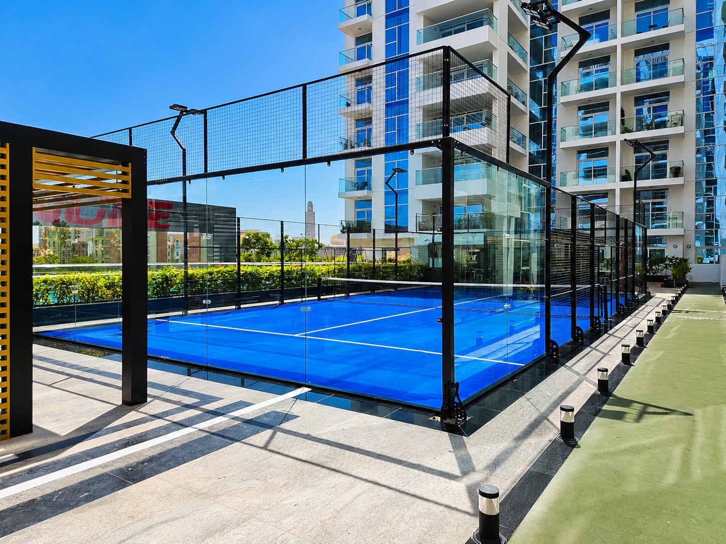 A tennis court with a glass enclosure, surrounded by a building with multiple balconies.