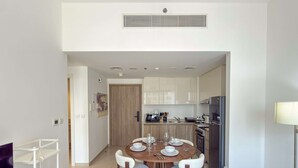 Uma área de refeições moderna com uma mesa redonda, cadeiras brancas e uma cozinha ao fundo.