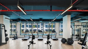Uma academia moderna com máquinas de cardio, pesos livres e amplas janelas com vista para área externa com mesas e cadeiras.