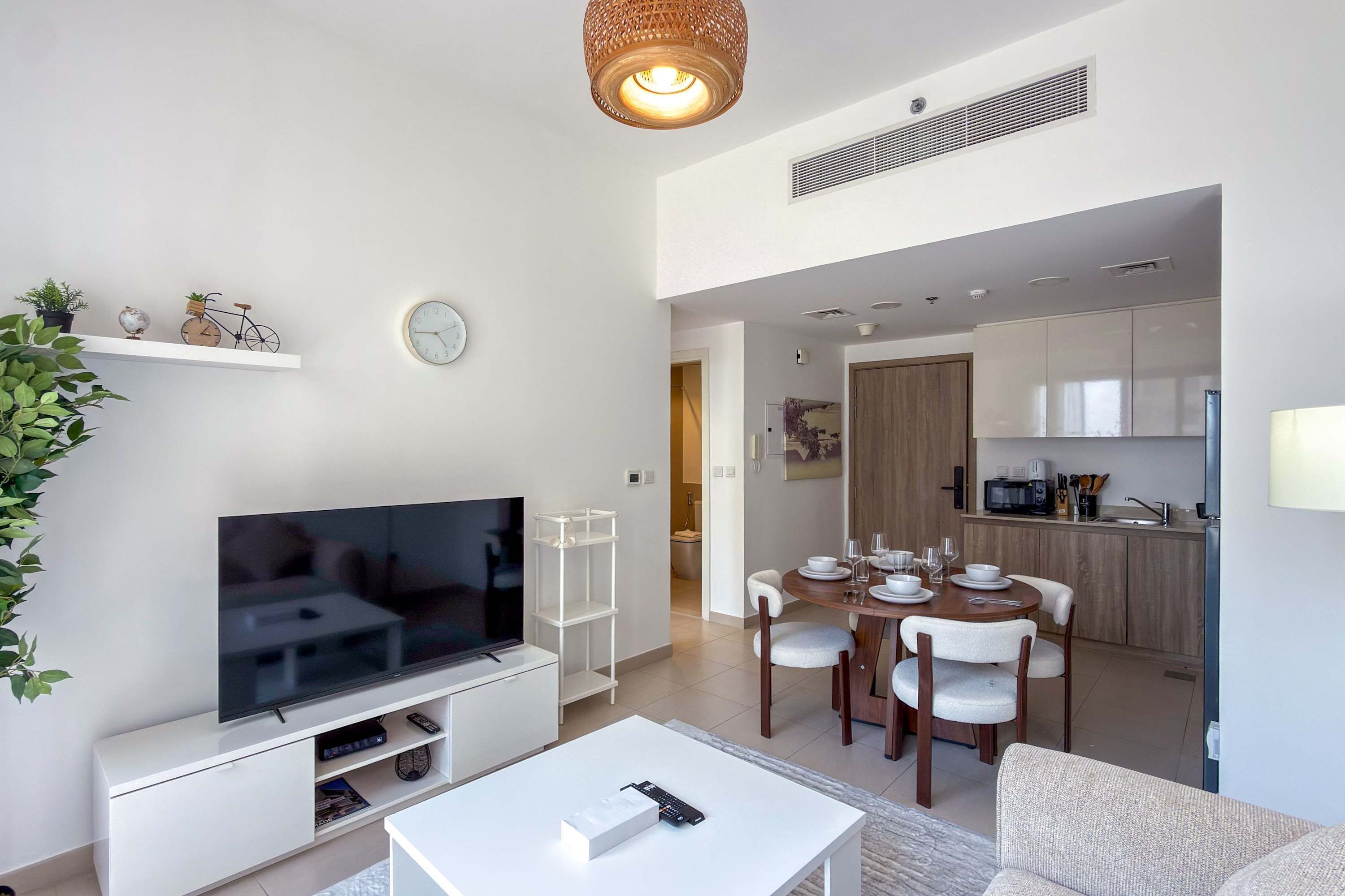 Ein modernes Wohnzimmer mit Flachbildfernseher, einem Essbereich mit Holztisch und Stühlen sowie einer Küche im Hintergrund.