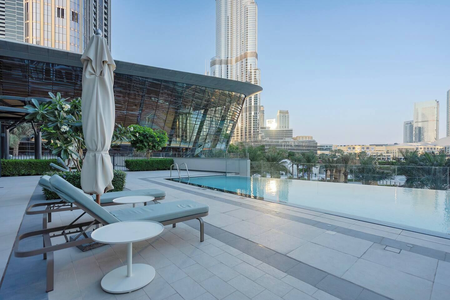 Un espace piscine aménagé sur le toit, avec des chaises longues et un coin salon couvert, offrant une vue panoramique sur la ville et ses bâtiments modernes.