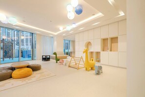 A modern living room with a large window, a sofa, a play area with a giraffe and elephant toy, and a bookshelf. - Luxury 1BR at Grande | Cityscape Views, Downtown (Dubai)