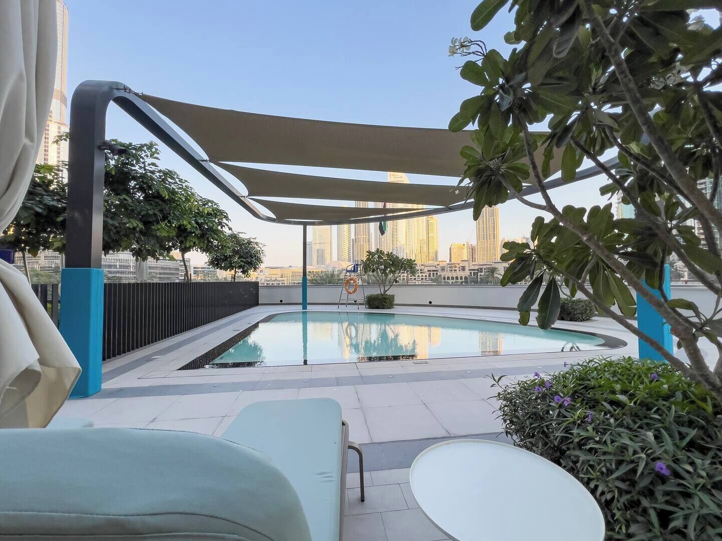 Une piscine sur le toit offrant une vue sur les gratte-ciel de la ville, entourée de chaises longues et protégée par un auvent.