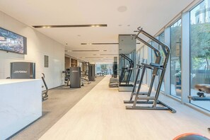 Une salle de sport moderne équipée de machines de cardio, d’appareils de musculation et d’un espace d’accueil avec un écran de télévision.