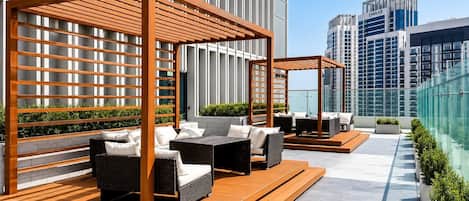 A rooftop terrace with outdoor seating, a wooden pergola, and a view of modern buildings.