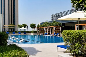 Ein Schwimmbecken mit Liegestühlen und Sonnenschirmen, umgeben von Grünflächen und modernen Gebäuden.