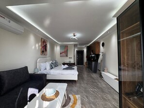 A modern hotel room with a bed, a sofa, a coffee machine, and a view of the hallway.