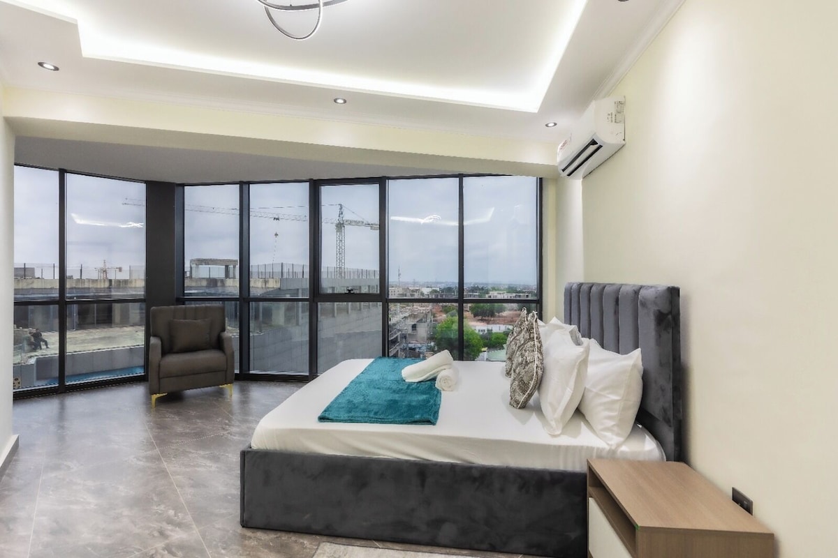 Un dormitorio moderno con una cama grande, un sofá y vistas a la ciudad a través de amplias ventanas.