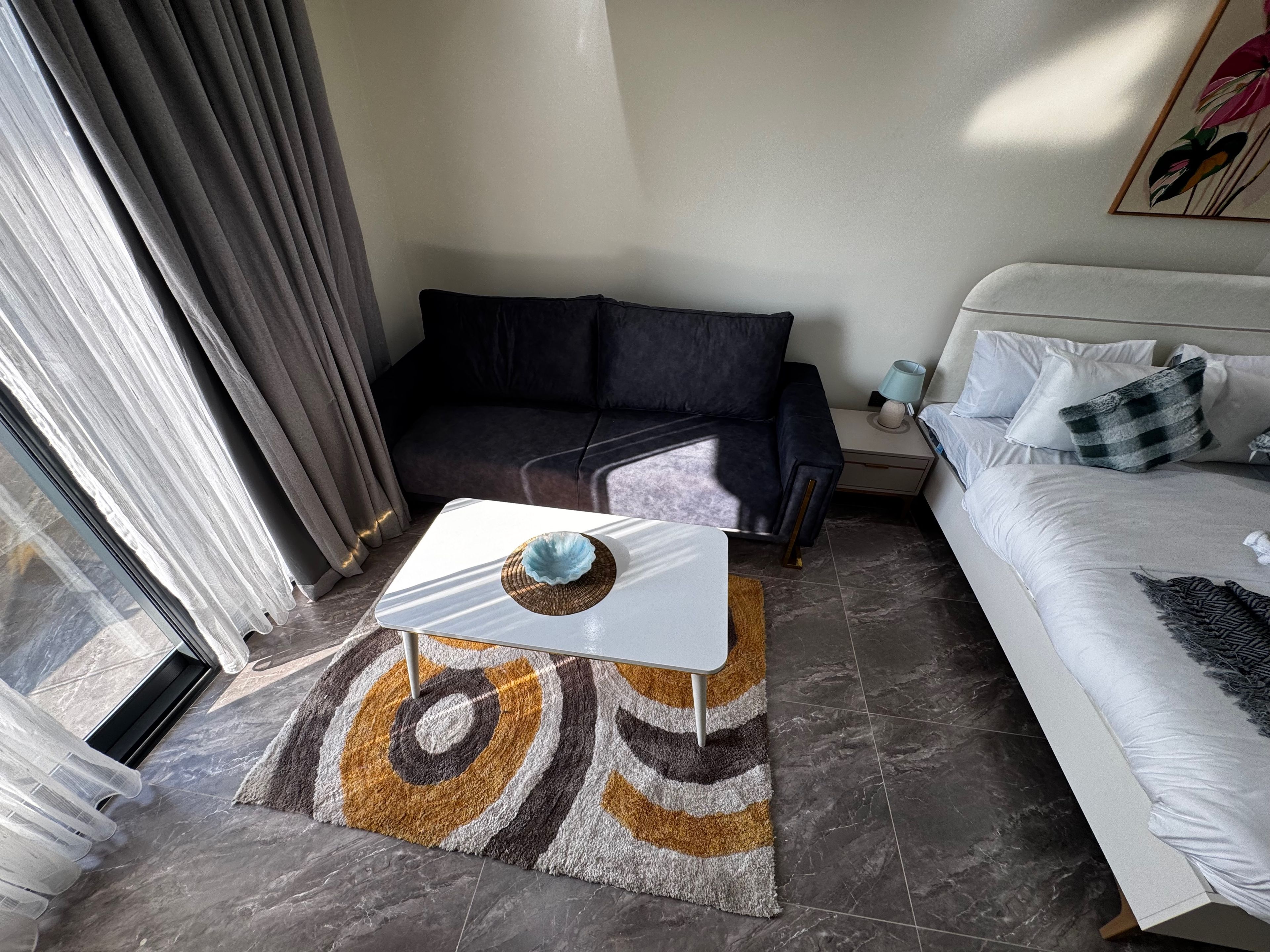 A modern hotel room with a sofa, a bed, a small table, and a patterned rug.