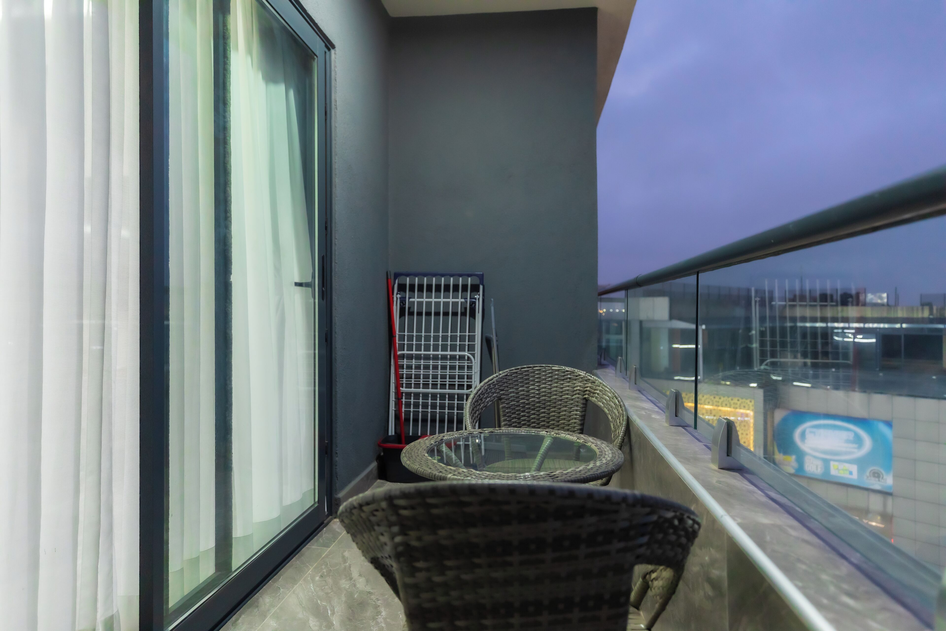 A balcony with a glass railing, a wicker chair, a small table, and a metal cart.