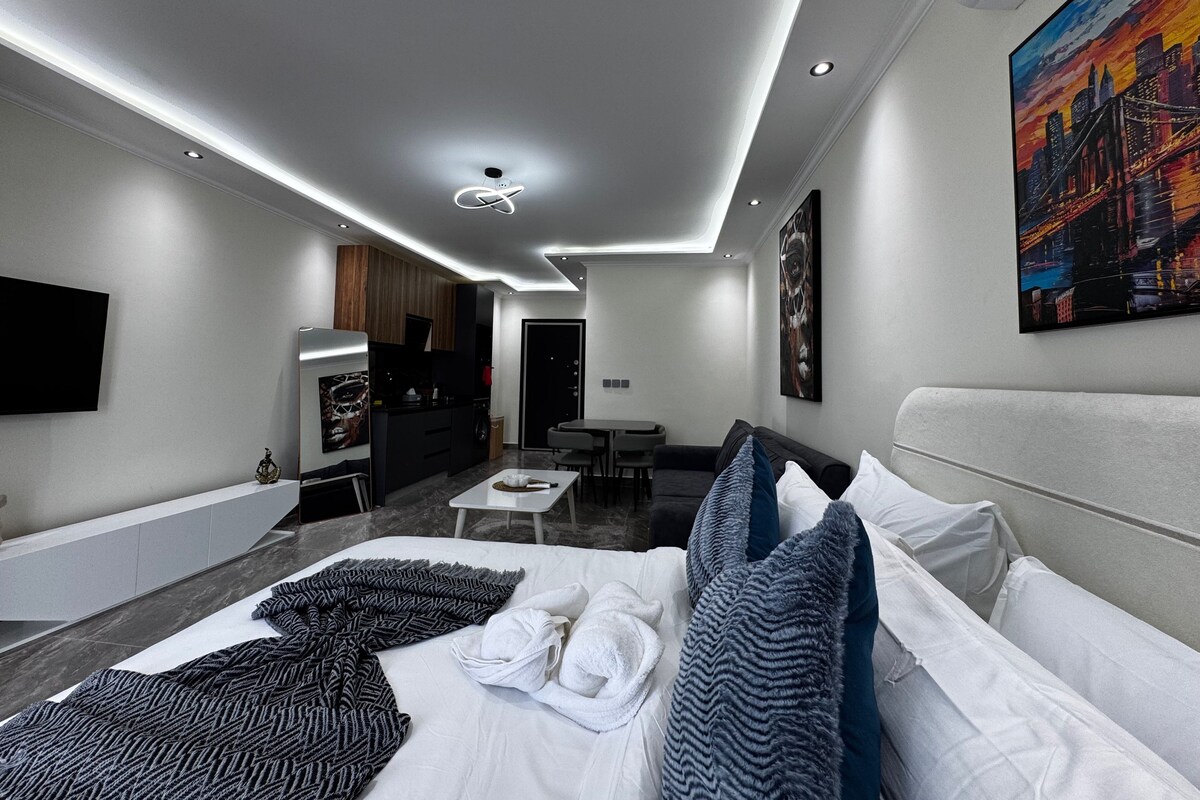 A modern hotel room with a bed, a desk, a seating area, and a painting on the wall.
