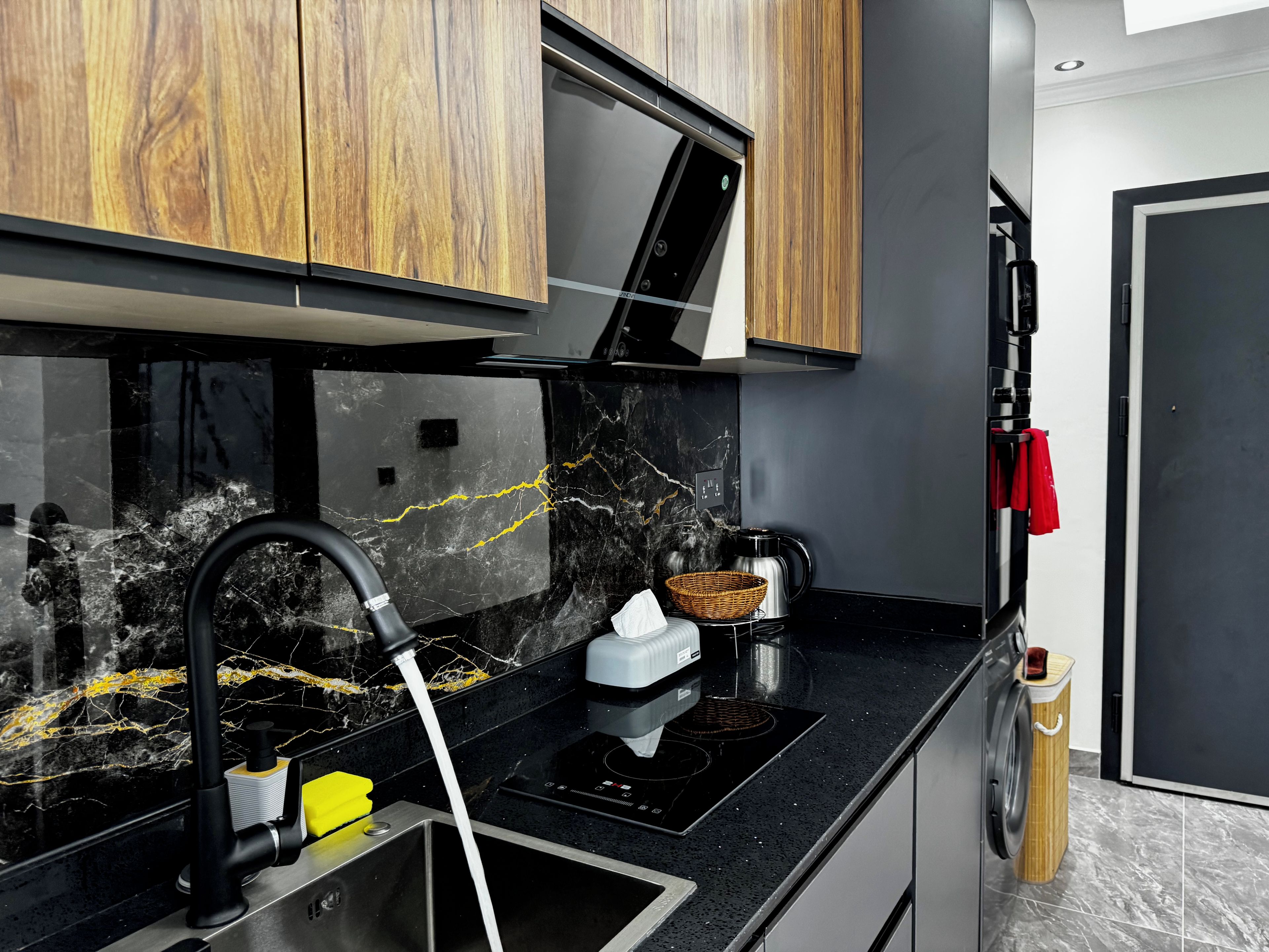 A modern kitchen with a black countertop, stainless steel sink, and wooden cabinets.