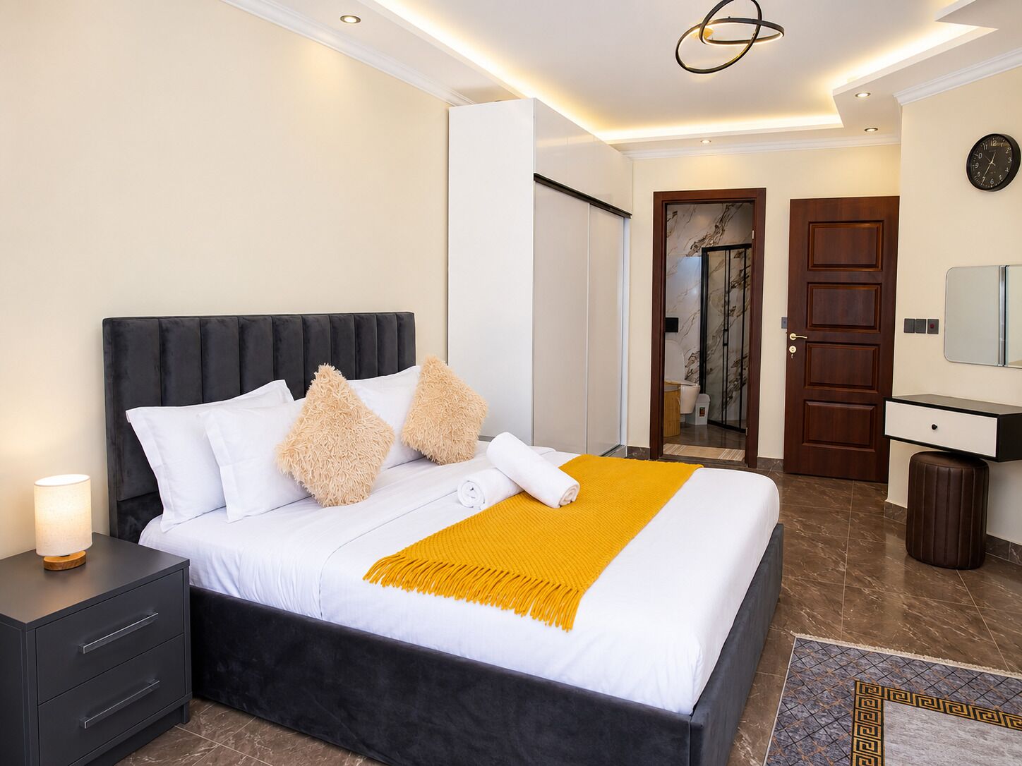 Una habitación de hotel moderna con una cama grande, una mesita de noche, un espejo y una puerta que da a un baño.