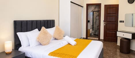 Una habitación de hotel moderna con una cama grande, una mesita de noche, un espejo y una puerta que da a un baño.