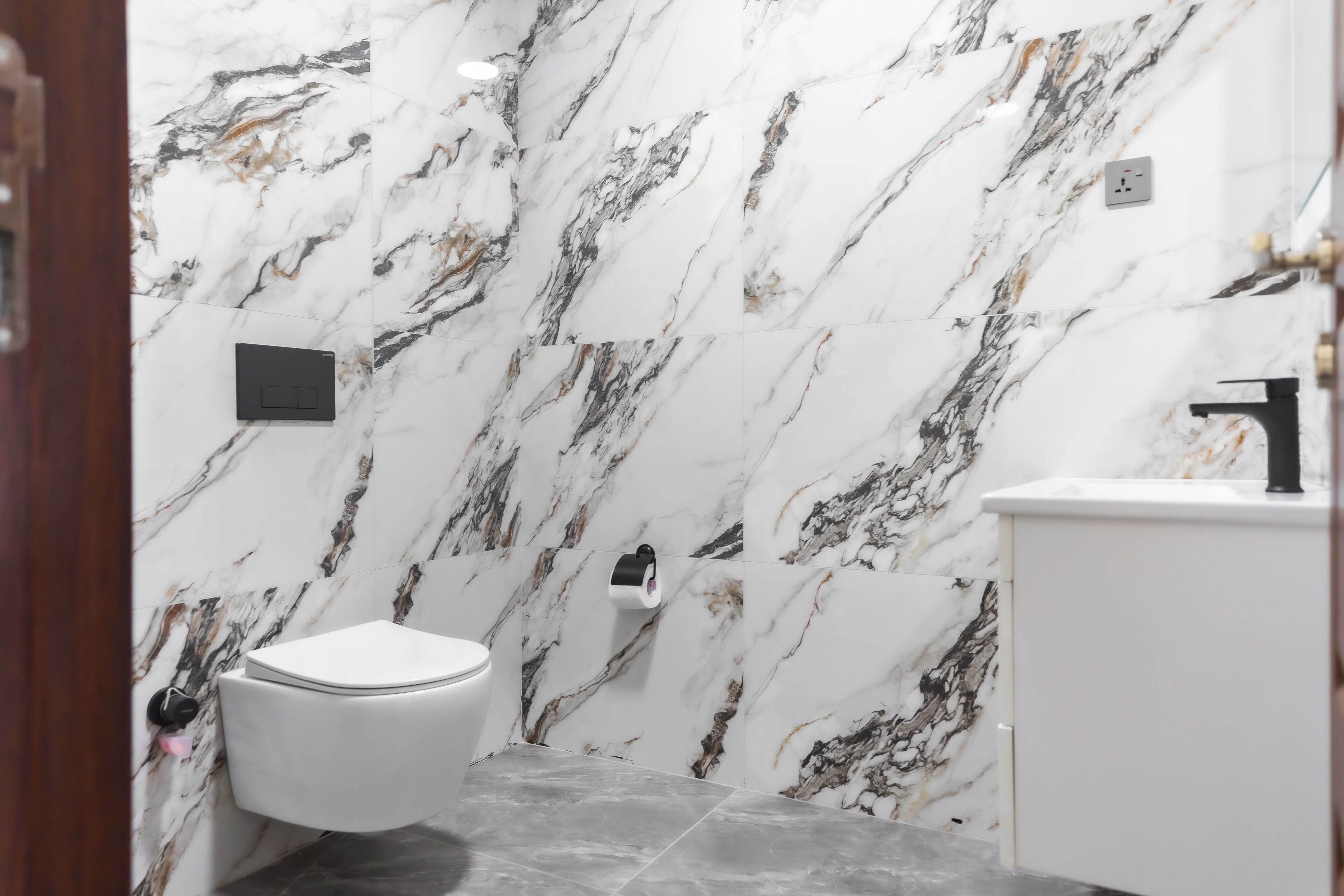 A bathroom with a toilet, a sink, and a marble wall.