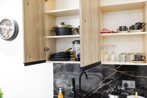 A kitchen with open wooden cabinets, a black marble backsplash, and various kitchenware. - Floria 807B (Accra)