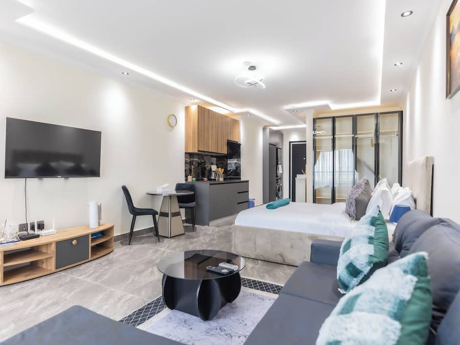 Una sala de estar moderna con sofá, mesa de centro, televisor y una cocina con alacenas y refrigerador.