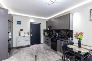 A modern kitchen with a dining area, featuring a black door, marble countertops, and a vase with flowers. - Floria 807B (Accra)