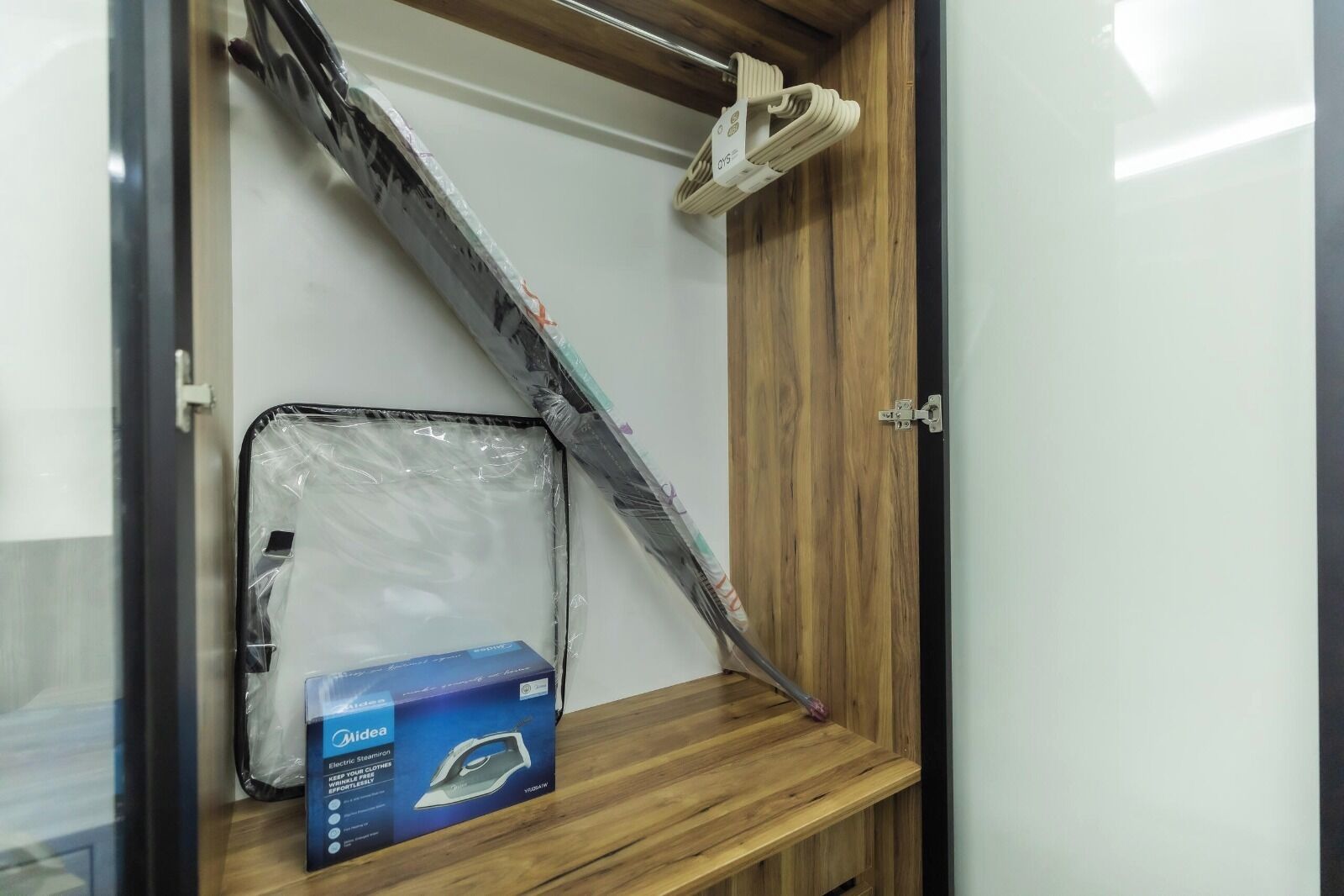 A room with a wooden door, a metal shelf, and a blue box labeled 'Midea Electric Steam Iron.'