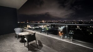 A balcony with a table and chairs, overlooking a cityscape at night.