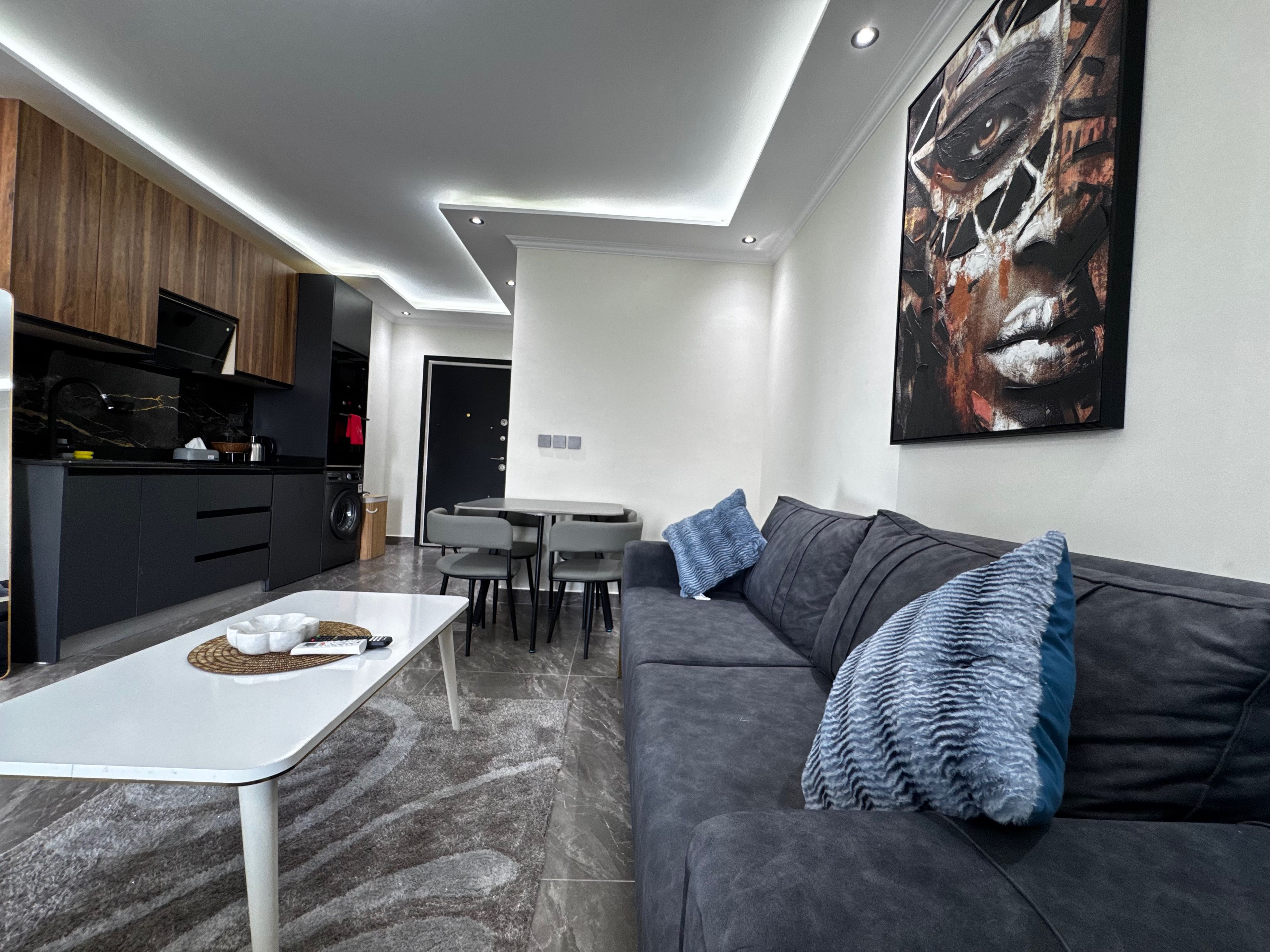 Ein modernes Wohnzimmer mit einem grauen Sofa, einem weißen Couchtisch und einem Essbereich mit schwarzem Tisch und Stühlen.