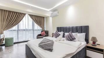 A modern hotel room with a large bed, a chair, a nightstand, and a view of the city.