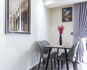 Un comedor con una mesa, sillas, un florero con flores, un cuadro en la pared y una ventana con cortinas.