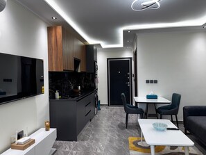 A modern kitchen with a built-in oven, a dining area with a table and chairs, and a living room with a sofa. - Floria 807B (Accra)