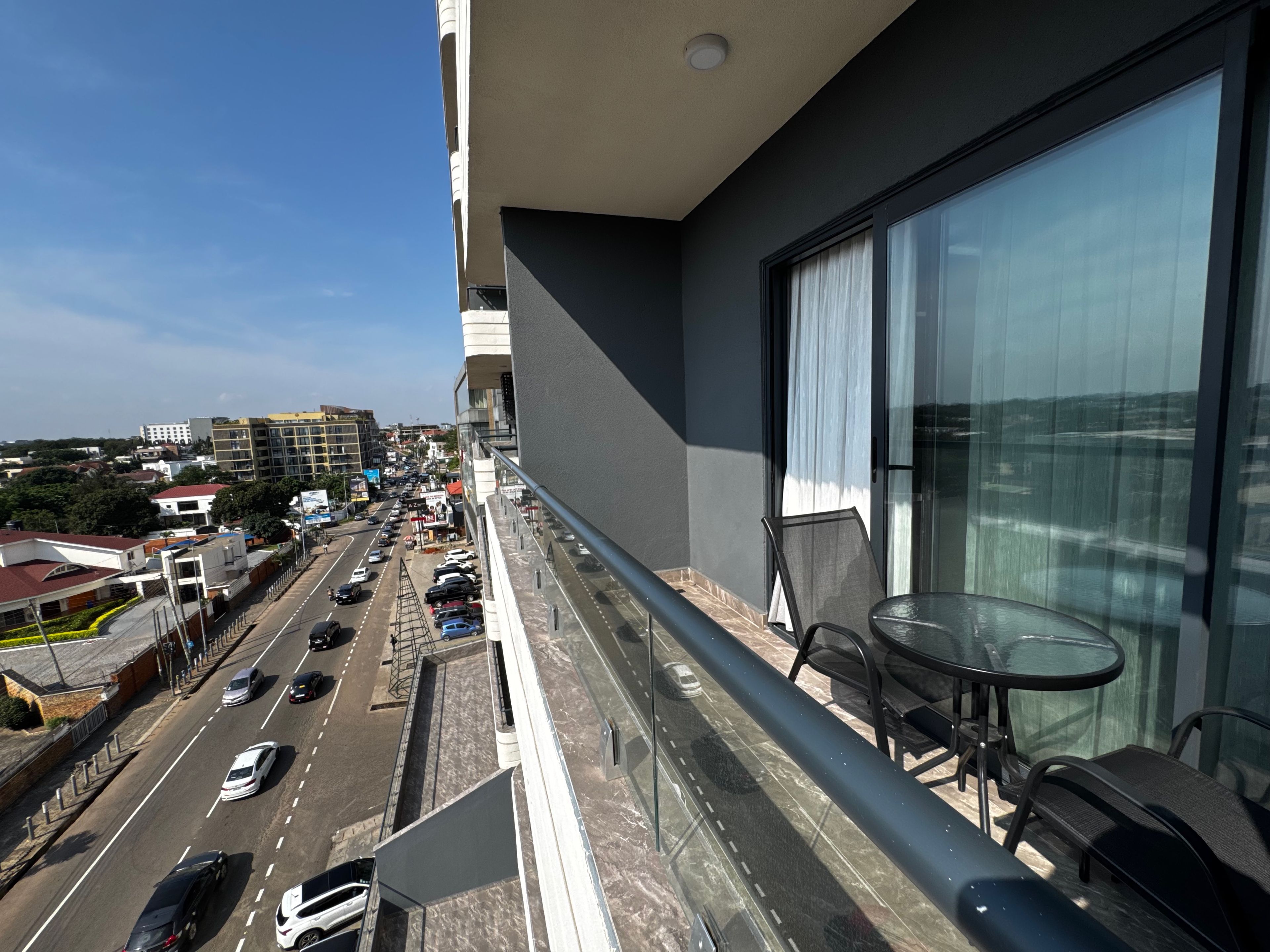 Un balcón con una mesa y sillas, con vista a una calle concurrida con coches y edificios.