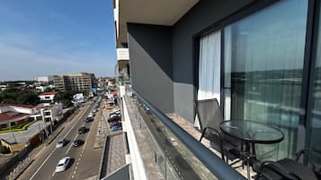 Un balcón con una mesa y sillas, con vista a una calle concurrida con coches y edificios.