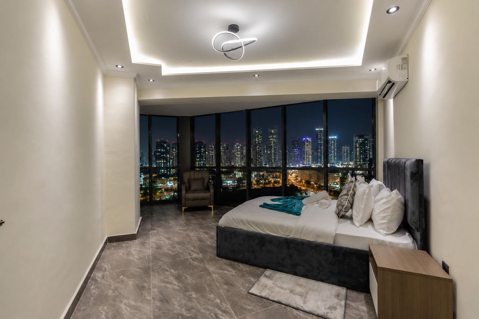 Ein modernes Schlafzimmer mit Blick auf die Stadt, einem großen Bett, einem Sessel und einem Schreibtisch.