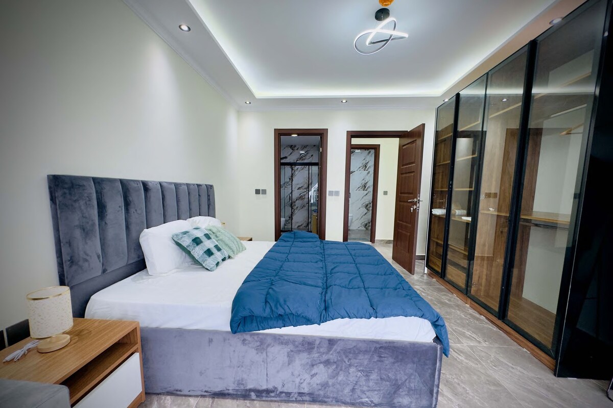 A modern bedroom with a large bed, a wardrobe, and a ceiling light fixture.