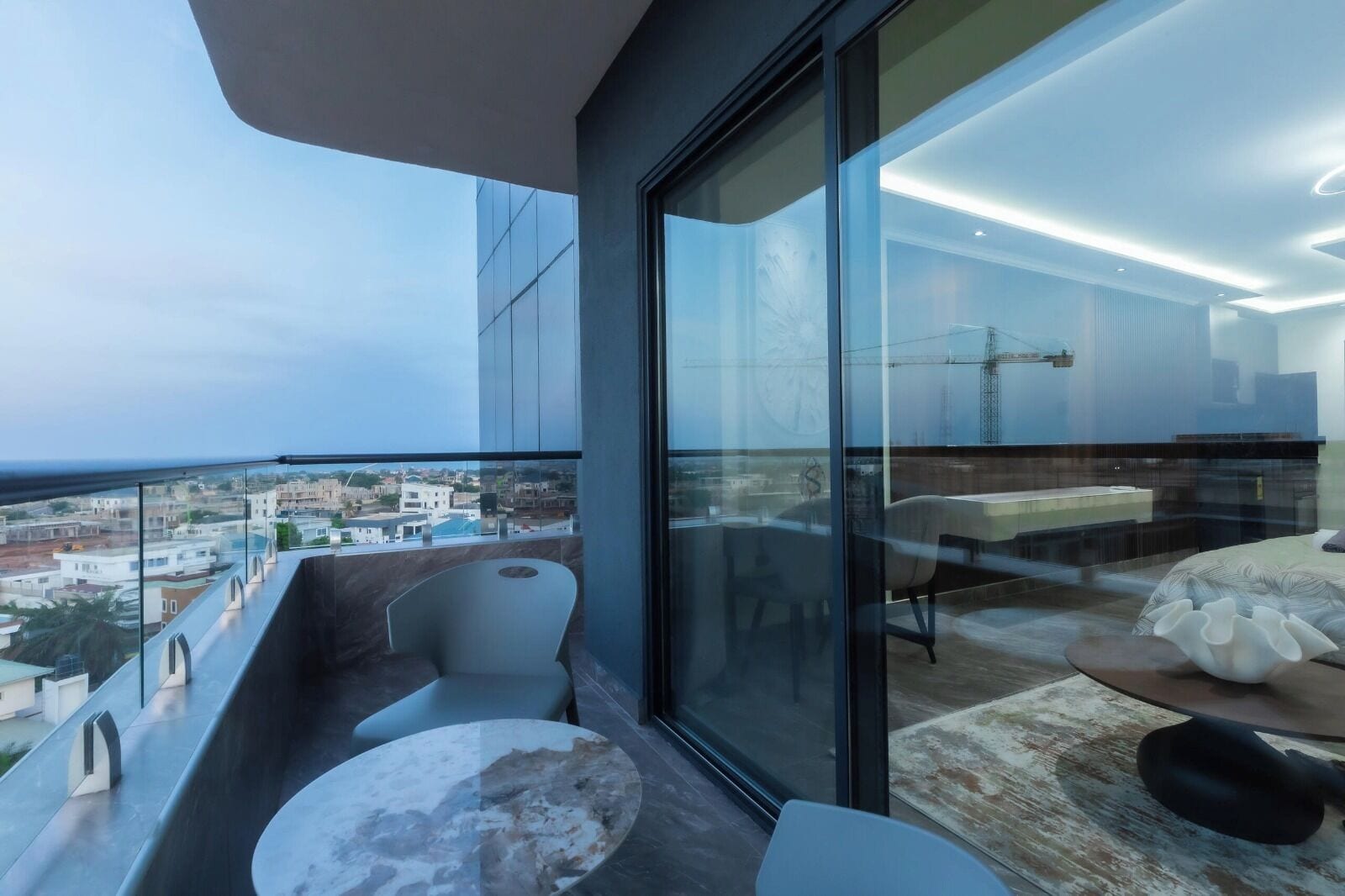 A modern balcony with a view of the cityscape, a dining area with a table and chairs, and a bedroom with a bed and a nightstand.