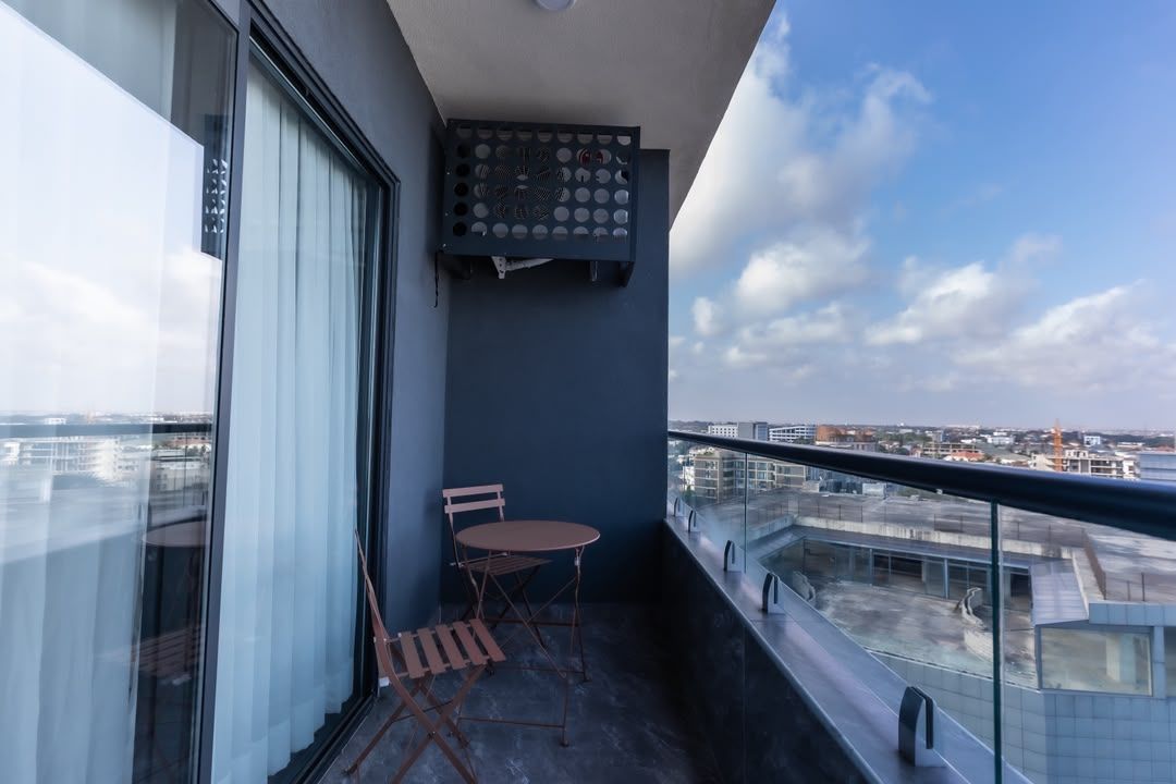En balkon med et bord og stole, udsigt over bybilledet og et vindue med skodder.