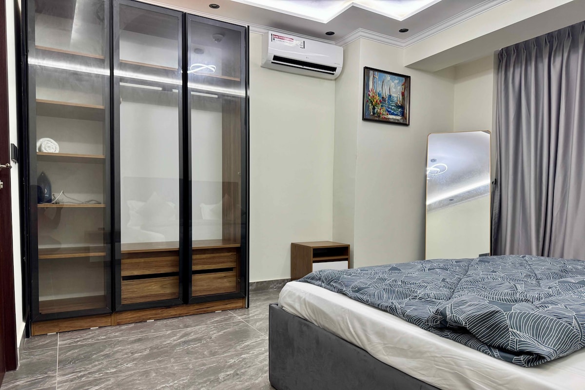 A bedroom with a bed, a wardrobe with glass doors, a small bedside table, and a painting on the wall.