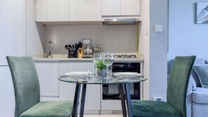 A compact kitchen with a dining area, including a glass table, chairs, and a stove. - Modern 1BR at Zada, High Floor & Pool View (Dubai)