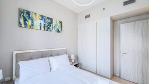 A bedroom with a bed, a nightstand, a wardrobe, and a painting on the wall. - Modern 1BR at Zada, High Floor & Pool View (Dubai)