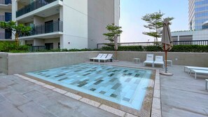 A rooftop swimming pool with lounge chairs and umbrellas, surrounded by a modern building with balconies. - Modern 1BR at Zada, High Floor & Pool View (Dubai)