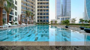 Una piscina con sillones y sombrillas, rodeada de palmeras y edificios modernos.